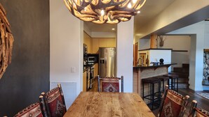 Un coin repas avec une table et des chaises en bois, un lustre et une cuisine en arrière-plan.