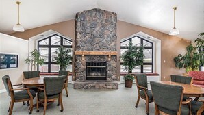 Una habitación amplia con chimenea de piedra, ventanas grandes y un comedor con muebles de madera.