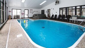 Una piscina interior con agua cristalina, rodeada de sillones de descanso y una escalera que lleva a un nivel superior.