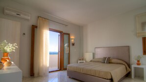 Una camera da letto con un letto grande, un comodino, una pianta in vaso e una porta scorrevole in vetro che dà su un balcone.