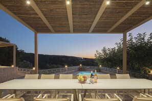 Un espace extérieur aménagé pour les repas, avec une piscine, entouré d’une clôture blanche et offrant une vue sur un paysage vallonné.