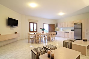 A modern kitchen with a built-in oven, a refrigerator, and a dining area with wooden chairs and a table. - Antigoni Villa, Spacious Nature Retreat with Pool (Rethymno, Crete)