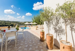 Une terrasse extérieure avec une piscine, des meubles blancs et des jardinières en terre cuite.
