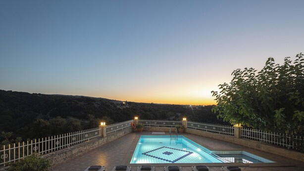 An outdoor swimming pool with a geometric tile pattern, surrounded by lounge chairs and a white fence.
