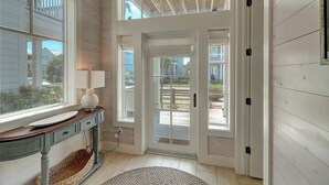 A hallway with a wooden floor, a lamp on a table, and a view of the outside through a glass door. - Cozy Beach Home in Cinnamon Shore w/ Easy Access to Resort Amenities (Port Aransas)