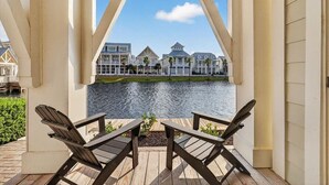 Eine Holzterrasse mit zwei Adirondack-Stühlen mit Blick auf ein Gewässer und eine Reihe von Häusern.