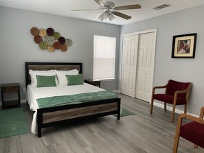 A bedroom with a bed, a ceiling fan, a window, a door, and a chair.