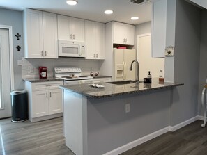 A modern kitchen with white cabinetry, a granite countertop, a stainless steel sink, and a built-in microwave.
