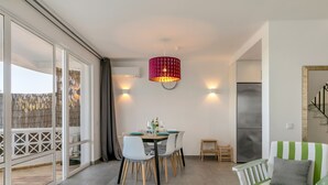 Ein Essbereich mit einem Tisch für vier Personen, einer roten Pendelleuchte und einem grün gestreiften Sofa.