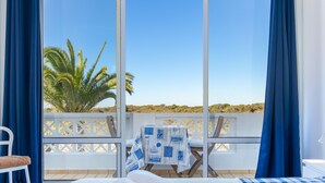 Ein Hotelzimmer mit einem großen Bett, einem Balkon mit Tisch und Stühlen sowie Blick auf Palmen und den Strand.