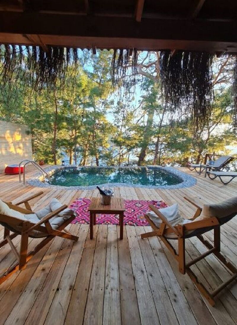 Um deck de madeira com piscina, espreguiçadeiras e uma mesa.