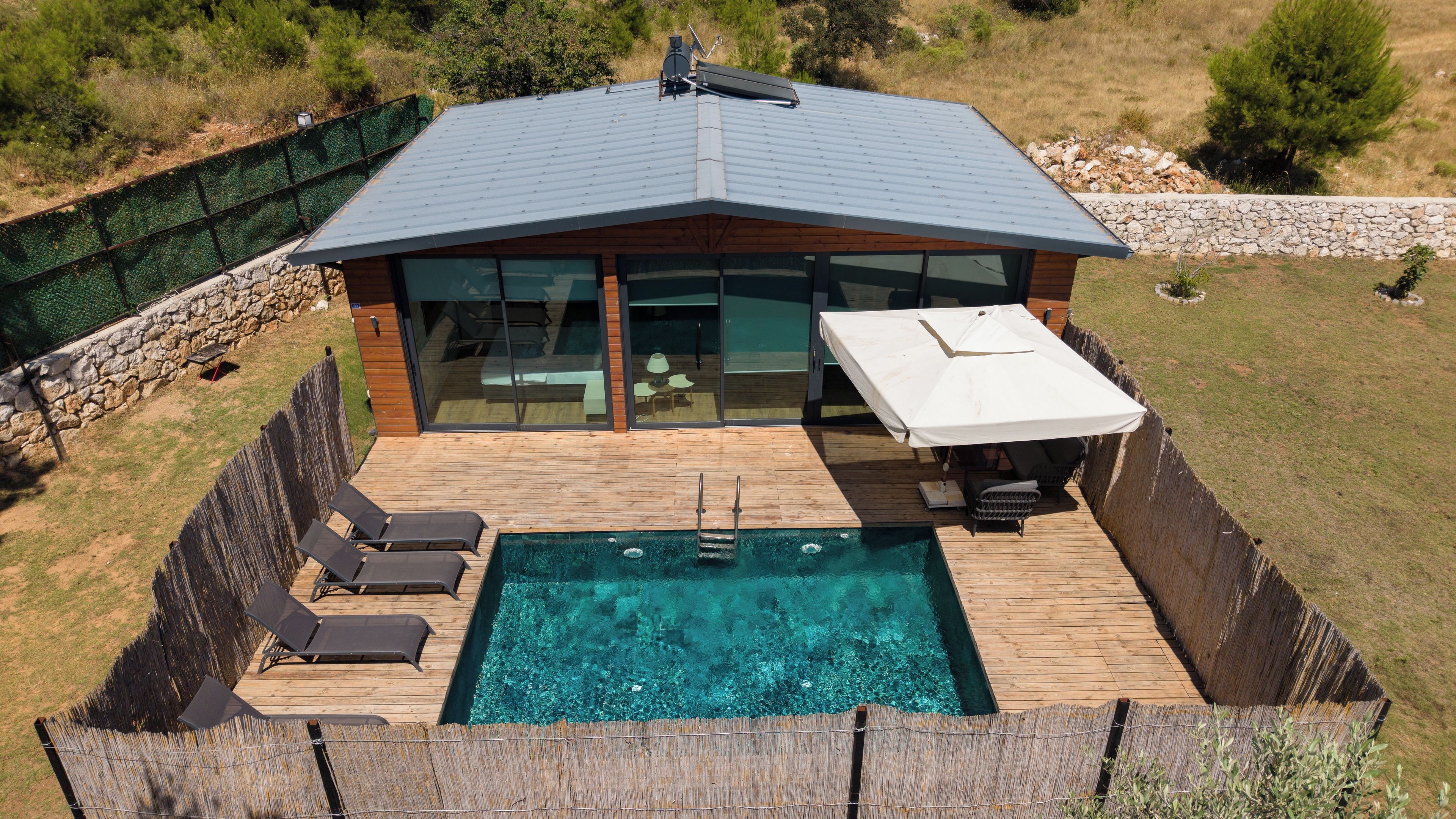 Ein modernes Haus mit Swimmingpool, Liegestühlen und einer glasüberdachten Terrasse.