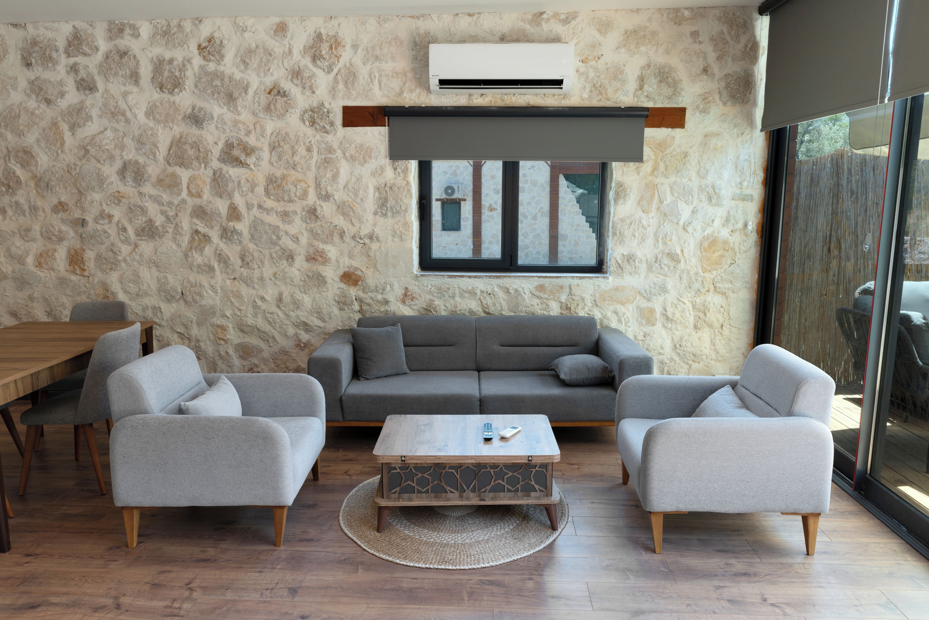 A living room with a stone wall, a grey sofa set, a wooden coffee table, and a dining table with chairs.