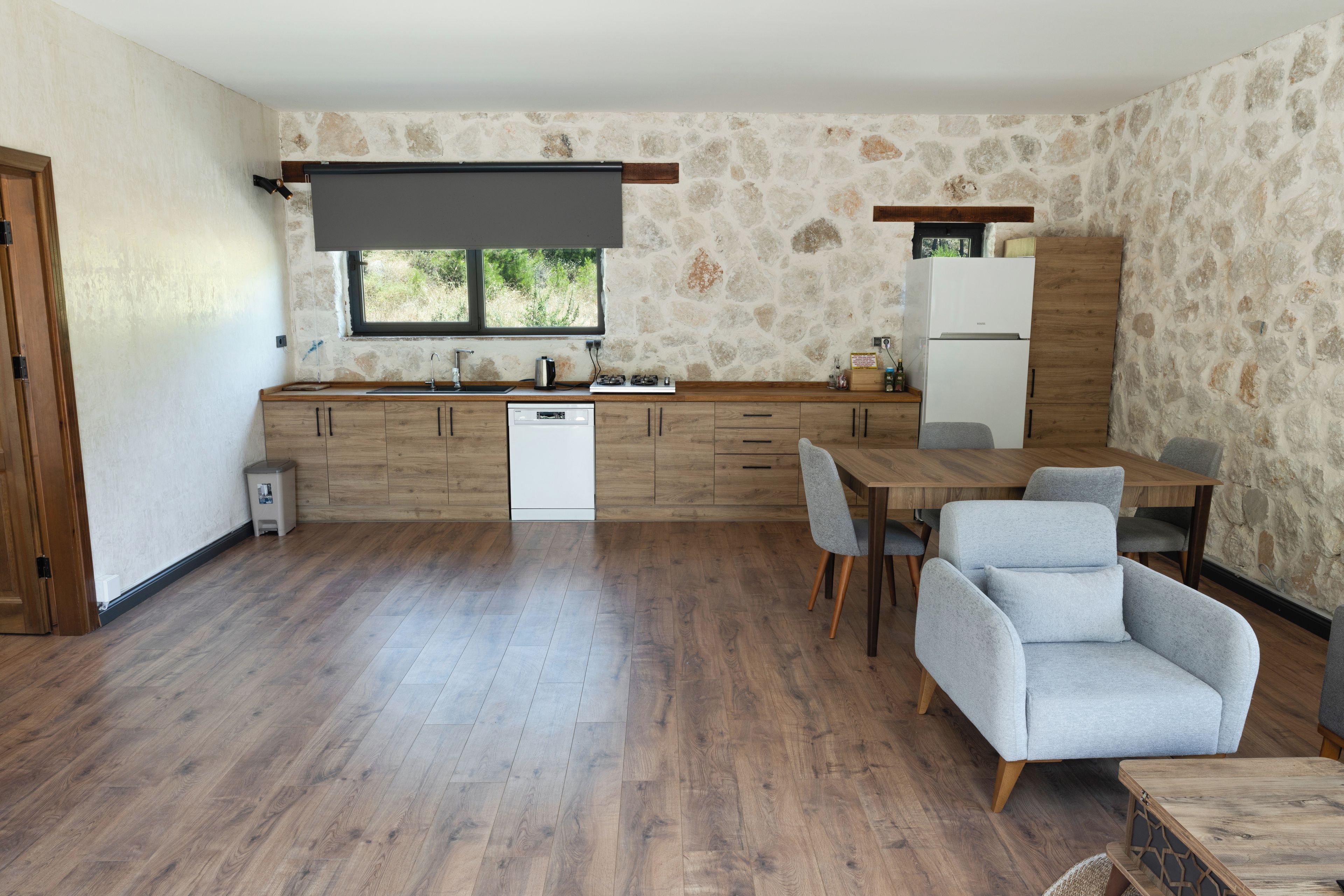 A modern kitchen with a stone wall, wooden cabinets, a built-in dishwasher, and a dining area with a table and chairs.