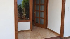 A room with a large window, a wooden door with glass panels, and a herringbone-patterned floor.