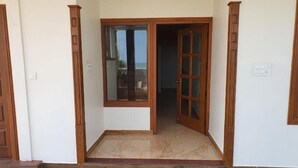 A room with a wooden door and a window, a tiled floor, and a white wall.