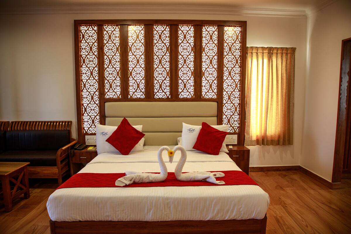 A hotel room with a large bed, a wooden headboard, a sofa, and a decorative partition.