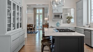 A modern kitchen with a central island, built-in cabinets, and a dining area with a view to the outdoors. - Stunning WC Home  | Private 6-Seat Golf Cart + Adult Bikes | Steps from Camp (Santa Rosa Beach)