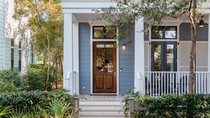 A two-story house with a front porch, a wooden door, and a small garden area. - Stunning WC Home  | Private 6-Seat Golf Cart + Adult Bikes | Steps from Camp (Santa Rosa Beach)