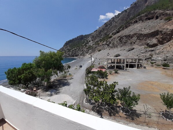 A coastal road with a building on a hillside, a beach, and a clear sky.
