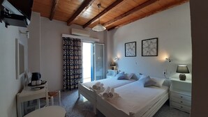 Quarto com teto de madeira, cama com almofadas, mesa de cabeceira com abajur, uma cadeira, pequena mesa com cafeteira e janela com cortinas.