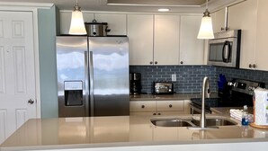 A modern kitchen with stainless steel appliances, a built-in oven, and a microwave. There are two pendant lights, a sink, and a bar stool.