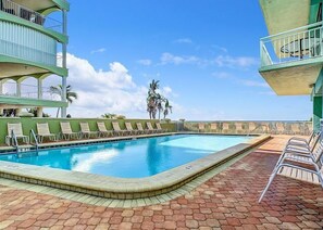 A swimming pool with lounge chairs, a brick patio, and a clear sky.
