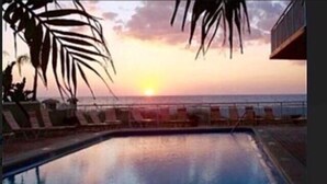 A swimming pool with lounge chairs and a sunset view.