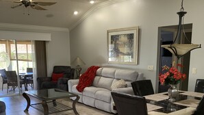 Un salon spacieux comprenant un canapé, une table à manger avec des chaises, un ventilateur de plafond et un tableau accroché au mur.