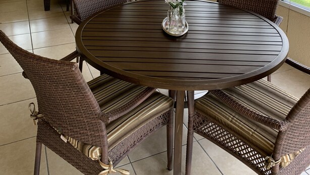 Une véranda avec une table ronde et des chaises en osier, de grandes fenêtres équipées de stores et un ventilateur de plafond.