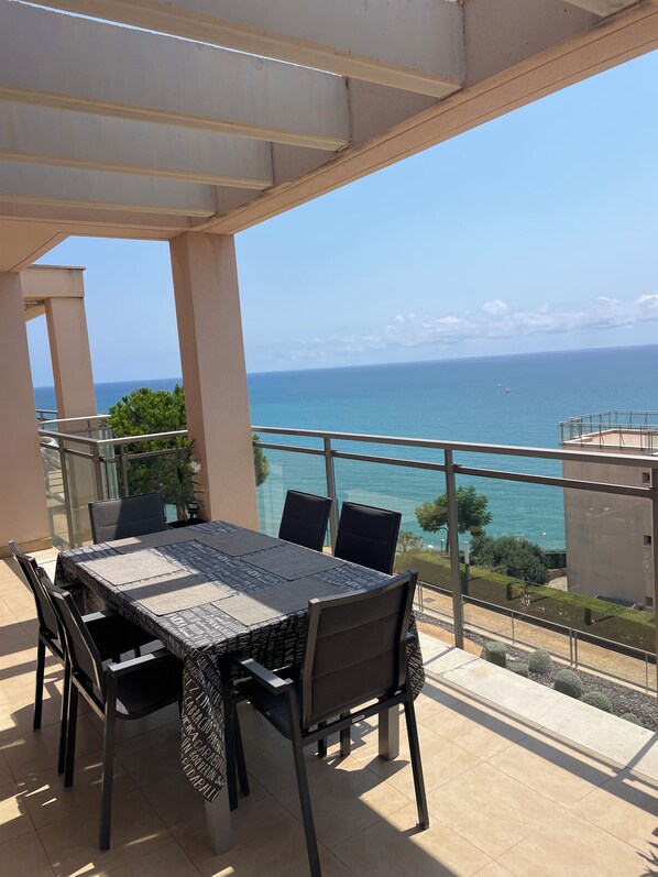 A balcony with a table and chairs, overlooking a clear blue sea and distant land.