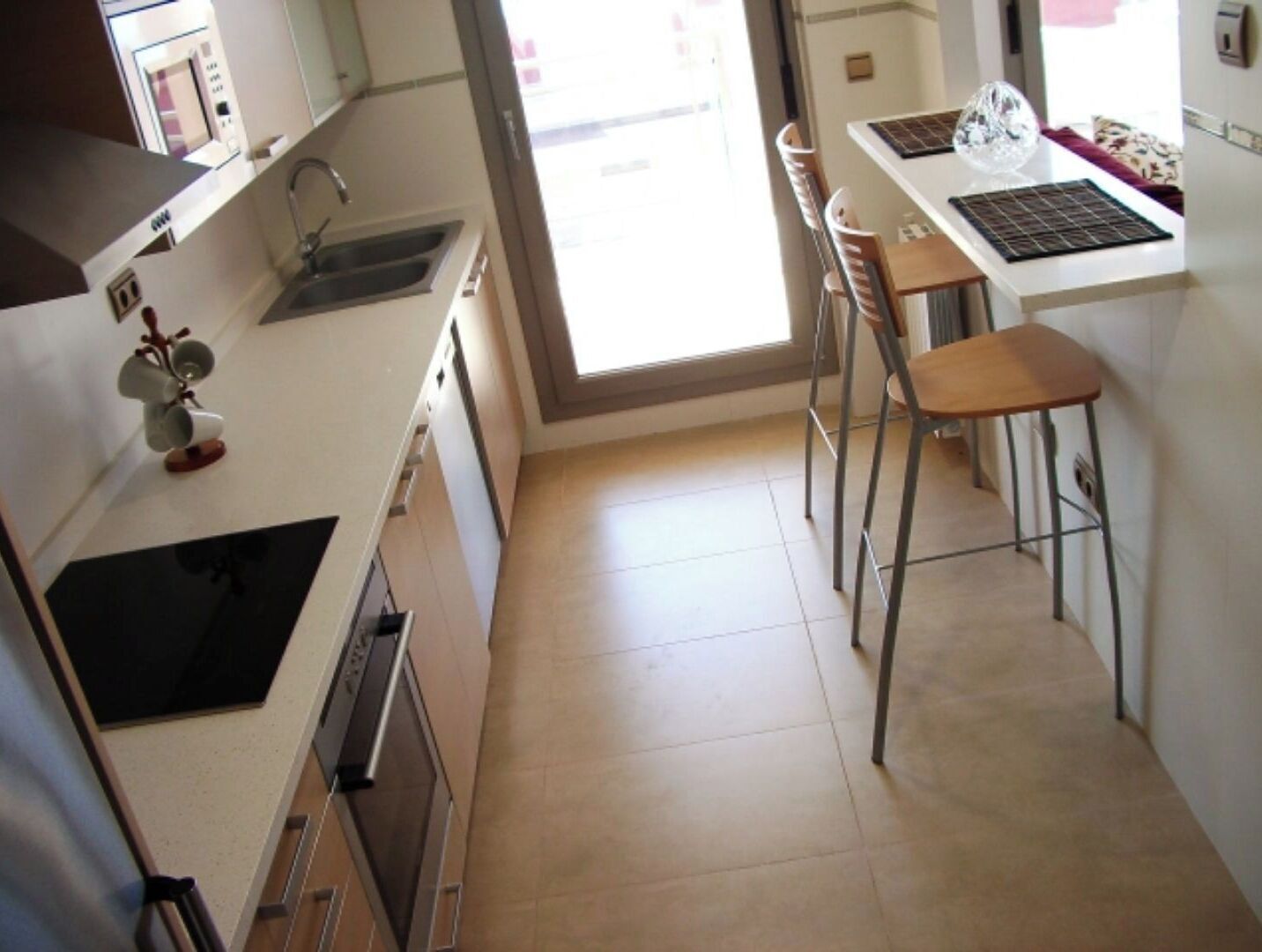 Een kleine keuken met een spoelbak, fornuis en een eethoekje met een stoel en tafel.