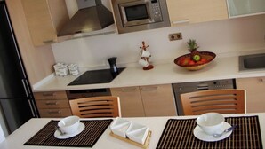 A modern kitchen with stainless steel appliances, wooden cabinets, and a dining area with a table set for two. - MODERN DUPLEX PENTHOUSE IN URB. LUXURY - SEA AND PINE FOREST VIEWS - SEA & PINES (Orpesa)