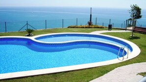 A swimming pool with a curved edge, surrounded by a fence, and overlooking a body of water. - MODERN DUPLEX PENTHOUSE IN URB. LUXURY - SEA AND PINE FOREST VIEWS - SEA & PINES (Orpesa)