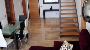 A modern living room with a glass dining table, white chairs, a red sofa, a wooden staircase, and a small black console table. - MODERN DUPLEX PENTHOUSE IN URB. LUXURY - SEA AND PINE FOREST VIEWS - SEA & PINES (Orpesa)