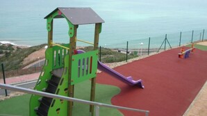 A playground with a slide and climbing structures, overlooking a beach and the sea. - MODERN DUPLEX PENTHOUSE IN URB. LUXURY - SEA AND PINE FOREST VIEWS - SEA & PINES (Orpesa)