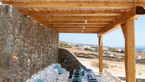 An outdoor seating area with stone walls and a wooden pergola, featuring white sofas and a table with chairs. - VENUS VIEW (Kalafati)