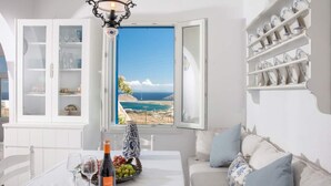 A room with a dining table set for two, a bottle of wine, and a fruit basket. A window with a view of the sea is visible. - VENUS VIEW (Kalafati)