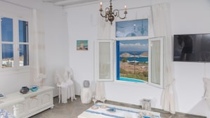 A room with a view of the sea, a chandelier, a table with decorative items, and a white sofa. - VENUS VIEW (Kalafati)