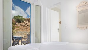 A hotel room with a bed, a door, and a view of a rocky landscape with greenery. - VENUS VIEW (Kalafati)