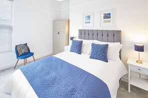 A bedroom with a bed, a chair, a bedside table, and a lamp.