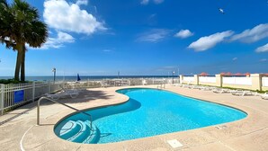 A swimming pool with a curved design, surrounded by lounge chairs and a palm tree. - The best location in Orange Beach - Ground floor condo - NEW to rental market (Orange Beach)