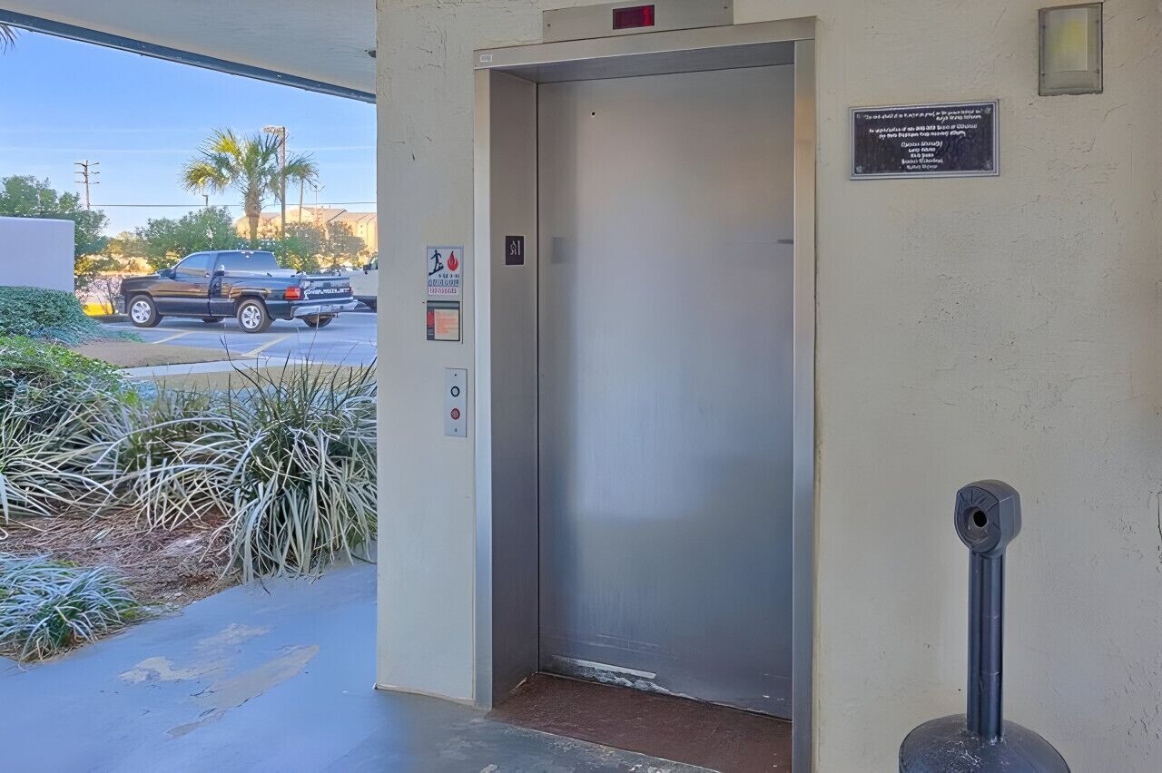 Entrada de ascensor con un letrero de estacionamiento, un extintor y una cámara de seguridad.