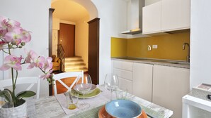 A modern kitchen with white cabinets, a yellow backsplash, and a dining area with a white table, chairs, and a vase of orchids. - L&D Suites 51, All Saints Square (Firenze)