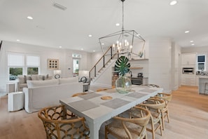 Una cocina moderna con armarios blancos, una isla central y un comedor con una mesa grande y sillas de mimbre.