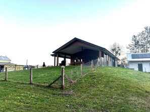 Un espace extérieur abrité, doté d’un toit, entouré d’une colline verdoyante et d’une clôture.