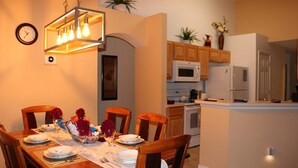 Zona pranzo con tavolo in legno apparecchiato per quattro persone, cucina moderna con elettrodomestici bianchi e lampadario decorativo sopra il tavolo.