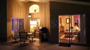 Un ambiente interno ben illuminato con zona pranzo, tavolo e sedie, una griglia e un lampadario.