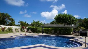 Una piscina con solárium de baldosas, sillas de descanso y una zona de estar cubierta.