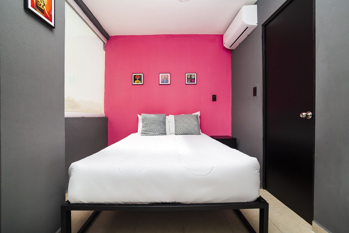 Un lit simple avec une literie blanche, un cadre en métal noir, un mur rose et trois petits tableaux accrochés au mur.
